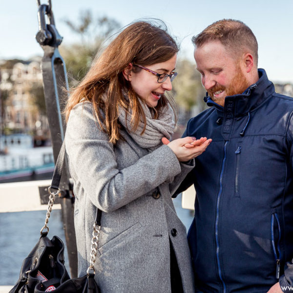 couple looks to the ring on a hand after a romantic proposal in Amsterdam. They stay on the bridge and smiling