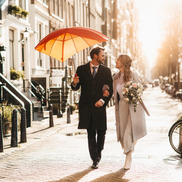 Married couple man and woman is walking with a red umbrella while wedding photographer in Amsterdam making pictures