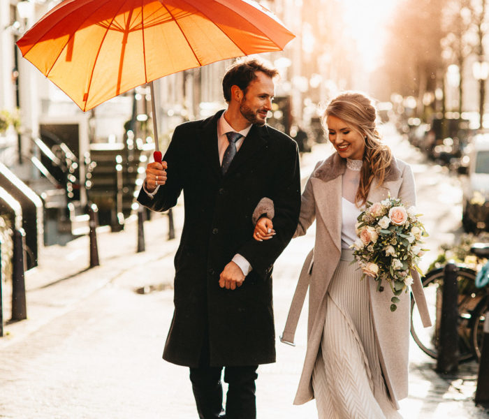 Wedding ouple with a red umbrella walking down the street of Amsterdam while photographer in Amsterdam taking pictures