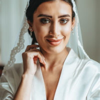 a portrait of a beautiful bride who smiles, touches her face and looks directly into the frame when she is being taken by a photographer in the Netherlands.