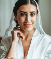 a portrait of a beautiful bride who smiles, touches her face and looks directly into the frame when she is being taken by a photographer in the Netherlands.