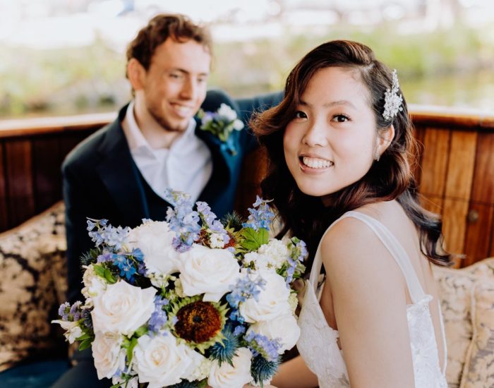 a beautiful bride sits on a chair and holds a bouquet of white roses in her hands, and the groom looks at her