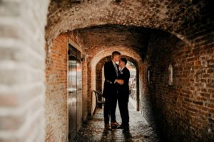 Gay wedding photoshoot picture made under the old bridge arch. Same sex couple stays and embrace.