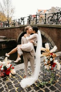 Wedding photoshoot in Amsterdam most iconic location at the bridge. Groom carries a bride on his arms