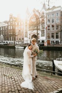 Beautiful wedding photoshoot in Amsterdam where couple staying in front of canal with sunset on background