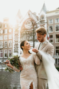 Couple poses for photographer during a wedding photoshoot in Amsterdam with a view on canal and houses