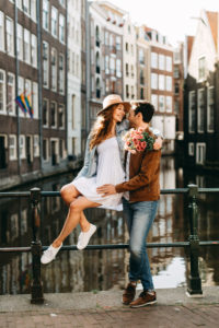 Engagement photoshoot in Amsterdam, where the girl sits on the handrail and boyfriend hugs her.