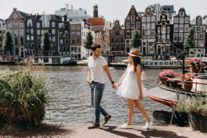 Couple walking at Amstel river with gingerbread houses background during their couple photoshoot in Amsterdam.
