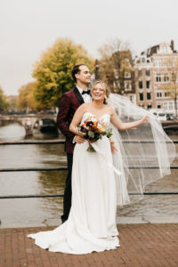 Happy couple in wedding gown stays on the bridge in Amsterdam. To learn more how to getting married in Amsterdam contact us for more information.