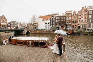Wedding in Amsterdam where couple stays on the pier in front of canal under the umbrella. Photographer captures their Amsterdam elopement.