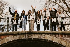 Romantic proposal in Amsterdam. The group of people staying on the bridge and holding Marry Me letters, while the couple riding on the boat during their boat proposal in Amsterdam. They chose Amsterdam proposal package to make this day memorable.
