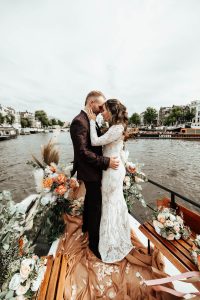 Smiling and happy wedding couple on a boat in Amsterdam, kissing each other, celebrating their elopement. Discover special elopement packages Amsterdam for your wedding in Amsterdam.