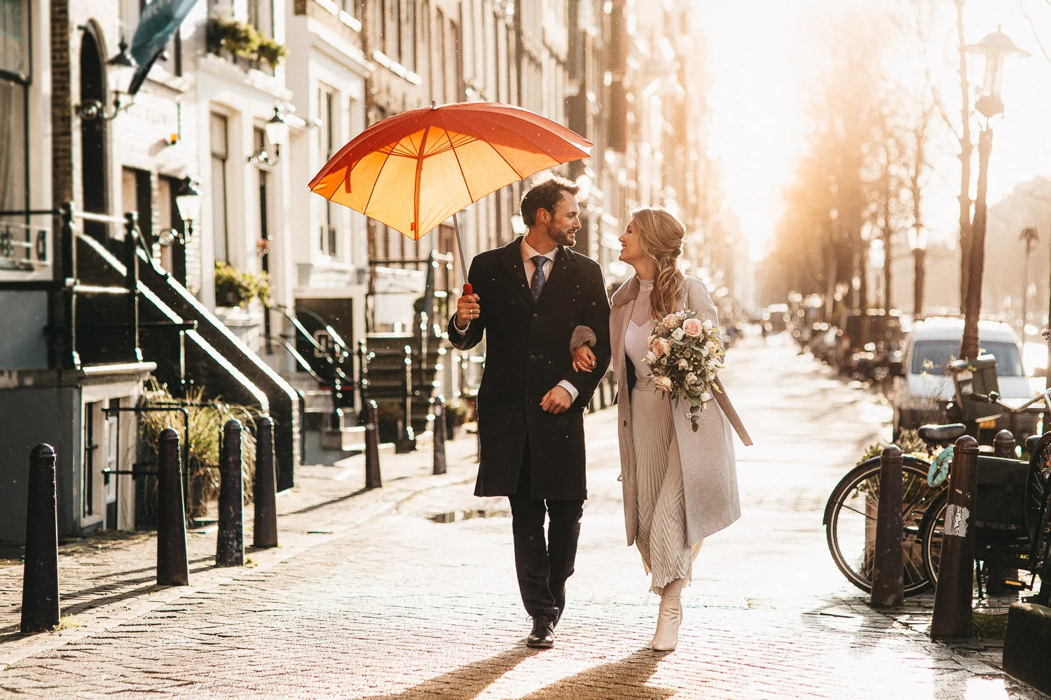 Married couple man and woman is walking with a red umbrella while wedding photographer in Amsterdam making pictures